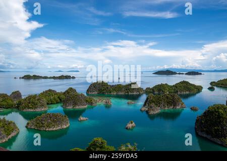 Aus der Vogelperspektive auf die üppig grünen Pianemo-Inseln in türkisfarbenem Wasser, mit Booten und fernen Inseln unter klarem Himmel, Fam-Inseln, Waigeo, Raja Ampat, West Stockfoto