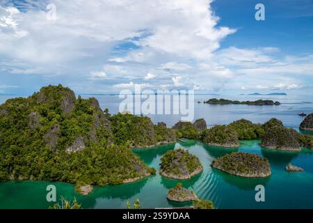 Aus der Vogelperspektive auf die üppig grünen Pianemo-Inseln in türkisfarbenem Wasser, mit Booten und fernen Inseln unter klarem Himmel, Fam-Inseln, Waigeo, Raja Ampat, West Stockfoto