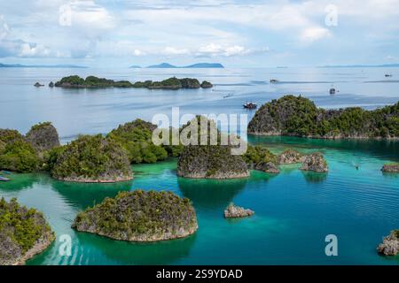 Aus der Vogelperspektive auf die üppig grünen Pianemo-Inseln in türkisfarbenem Wasser, mit Booten und fernen Inseln unter klarem Himmel, Fam-Inseln, Waigeo, Raja Ampat, West Stockfoto