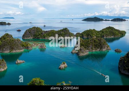 Aus der Vogelperspektive auf die üppig grünen Pianemo-Inseln in türkisfarbenem Wasser, mit Booten und fernen Inseln unter klarem Himmel, Fam-Inseln, Waigeo, Raja Ampat, West Stockfoto