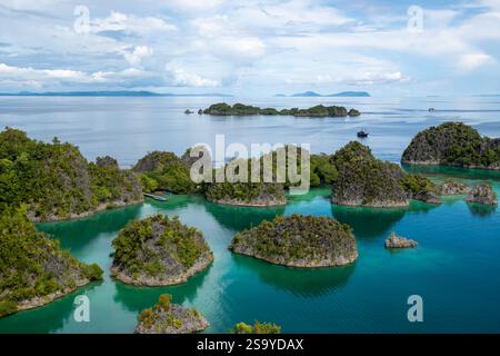 Aus der Vogelperspektive auf die üppig grünen Pianemo-Inseln in türkisfarbenem Wasser, mit Booten und fernen Inseln unter klarem Himmel, Fam-Inseln, Waigeo, Raja Ampat, West Stockfoto