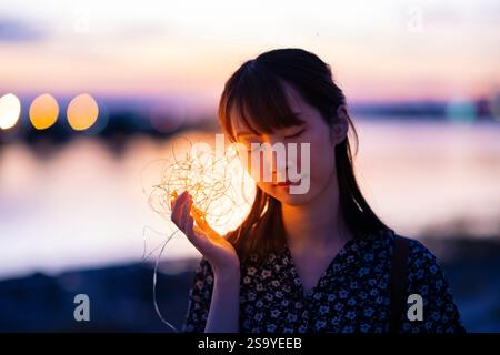 Eine junge Frau, die Licht nahe am Ohr hält Stockfoto