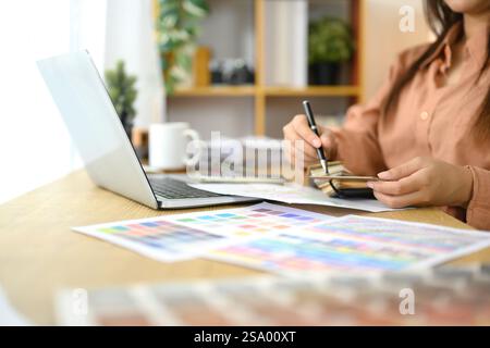 Zugeschnittene Aufnahme einer Designerin, die Farbmuster und Designmaterialien am Schreibtisch analysiert Stockfoto