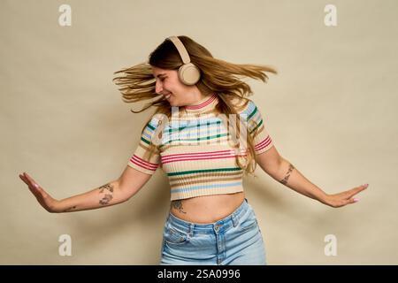 Sorglose junge Frau, die Musik mit kabellosen Kopfhörern genießt, mit fließenden Haaren tanzt und Freude und Freiheit ausdrückt Stockfoto
