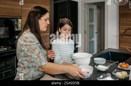 Mutter und Tochter bereiten Zutaten für den Kuchen in der modernen Küche vor Stockfoto