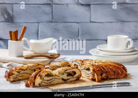 Süßer Zimt geflochtener Loaf mit Perlzucker auf Schneidebrett auf weißem Holztisch mit Backsteinwand im Hintergrund, Kaneli Pullapitko, finnische r Stockfoto