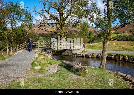 Menschen, die über eine Fußgängerbrücke über Buttermere Dubs in der Nähe des Sees im Herbst Lake District National Park Cumbria England Großbritannien spazieren Stockfoto