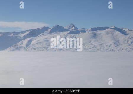 Ein atemberaubender Blick auf die schneebedeckten Aragats-Gebirgszüge in MyLer, Armenien, die sich über einem Wolkenmeer unter einem klaren blauen Himmel erheben Stockfoto