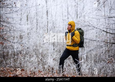 Wandern im Winterwald. Wandermann in gelber Jacke mit Rucksack, der durch frostiges Waldland läuft Stockfoto