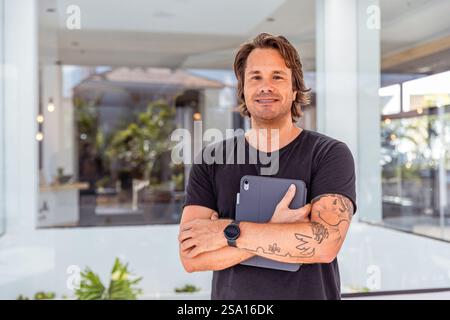 Ein Mann mit Tätowierungen am Arm hält eine Tafel in den Händen. Er lächelt und ist stolz und glücklich. Stockfoto