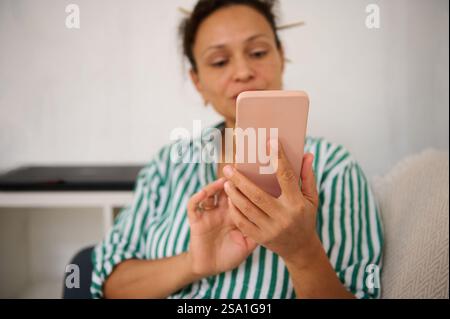 Eine Person konzentriert sich auf ihr Smartphone, während sie bequem sitzt und in einem hellen Raum mit ihrem Gerät interagiert. Stockfoto