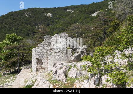 Steinruinen in einem bewaldeten Berggebiet unter einem klaren blauen Himmel umgeben von grünen Bäumen, Kirche des Heiligen Geistes, BaTka, Baska, Insel Krk, Kvarn Stockfoto