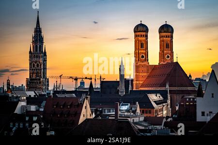 Ein atemberaubender Blick auf den Sonnenuntergang über München mit den berühmten Türmen der Frauenkirche und dem Neuen Rathaus. Der Himmel ist in warmen Orange-Tönen gemalt Stockfoto
