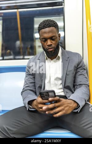 Junger Geschäftsmann, der in einer U-Bahn sitzt, mit einem Smartphone surft, E-Mails liest und während der Fahrt in Verbindung bleibt Stockfoto