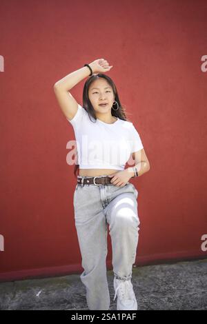 Vertikales Foto einer asiatischen Teenagerin, die K-Pop auf der Straße vor einer roten Wand tanzt Stockfoto