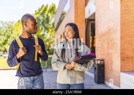 Zwei afrikanische und chinesische multiethnische Freunde unterhalten sich auf dem Universitätsgelände mit Mappen und Notizbüchern Stockfoto
