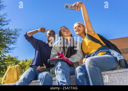 Gruppe lächelnder multiethnischer Studenten, die Selfie machen, die an einem sonnigen Tag vor dem Campus sitzen Stockfoto