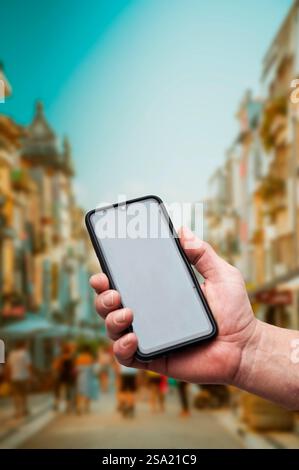 Hand in der Hand, die ein Smartphone mit leerem Bildschirm hält, in einer Straße in der Stadt Stockfoto