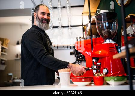 Professioneller Barista in schwarzer Schürze, der im Restaurant arbeitet. Porträt glücklicher Barkeeper, die in seiner Bar Kaffee machen. Stockfoto