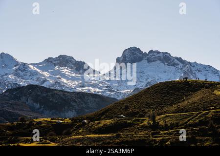 Schneebedeckte Berge in der Ferne, ein grasbewachsener Hügel im Vordergrund und ein paar Autos parkten entlang einer Straße. Stockfoto