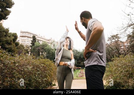 Ein Wellnesstrainer und Trainee nehmen an einer fröhlichen und unterstützenden Fitnessaktivität im Freien Teil und bringen ihre Begeisterung und Motivation zum Ausdruck. Stockfoto