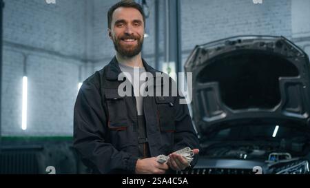 Glücklicher Mann kaukasischer bärtiger lächelnder männlicher professioneller Mechaniker Servicemanager Autoingenieur Autodienstleister technischer Arbeiter, der sich im Reparaturfahrzeug ausgibt Stockfoto