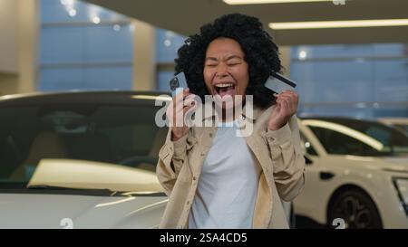 Afroamerikaner glücklicher Kunde weibliche Käuferin halten Kreditkarte Handy Shopping kaufen neue Luxus-Elektroauto im Autohaus des Autohauses Stockfoto