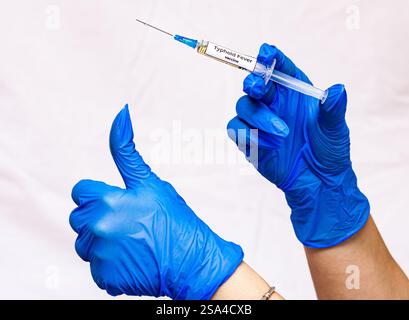 Nahaufnahme der Hand des weiblichen Arztes in blau sterilisierten chirurgischen Handschuh mit medizinischer Plastikspritze gefüllt mit blauem Medikament vor weißem Hintergrund Stockfoto