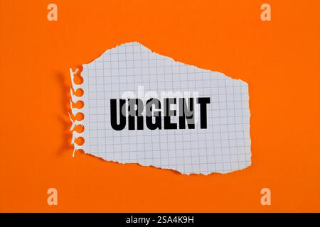 Dringende Nachricht auf gerissenem, kariertem Papier mit orangefarbenem Hintergrund. Konzeptionelles dringendes Wortsymbol. Kopierbereich. Stockfoto