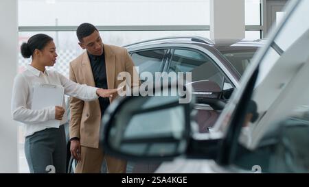 Afroamerikanische Frau Verkäufer Händler Beratung in Auto-Showroom helfen Mann Kunde wählen neues Auto modernes Elektroauto Verkäufer Consult Stockfoto
