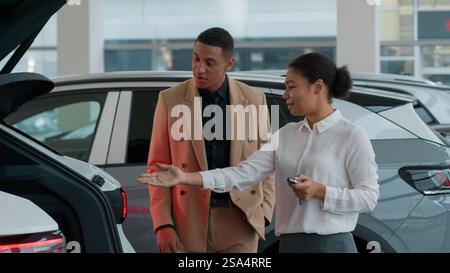 Afroamerikanische Frau Händlerverkäufer helfen Mann Kunde im Autohändlergeschäft Verkäuferin Consult zeigt automatische Kofferraumöffnungsfunktion von elektrisch Stockfoto