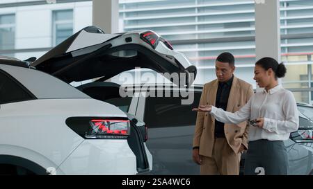 Afroamerikanische Autohändlerin Verkäuferin hilft Kunden Geschäftsmann Käufer im Showroom zu demonstrieren automatische Kofferraumöffnung neue Funktion des Elektroautos Stockfoto