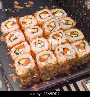 Sushi-Brötchen mit frischem Gemüse und cremiger Füllung sind kunstvoll auf einem Schieferbrett angeordnet. Das goldfarbene, knusprige Äußere verleiht dem Look einen einladenden Touch Stockfoto