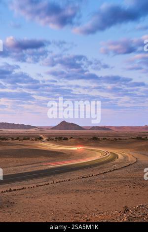 Leichte Pfade vorbeifahrender Autos auf der Straße nach Sossusvlei, frühmorgens blaue Stunde. Himmel mit flauschigen Wolken. Sesriem, Nationalpark, Namibia, Afrika. Stockfoto
