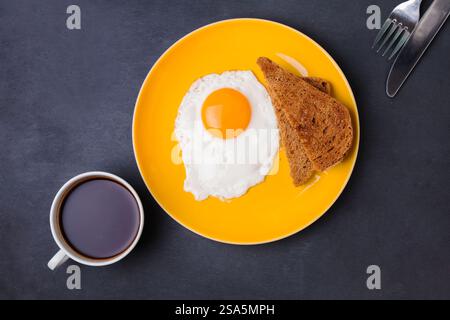 Frühstück mit sonnigem Ei, Toast und Kaffee auf einem leuchtend gelben Teller, Blick von oben Stockfoto