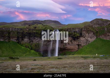 Aus der Vogelperspektive des majestätischen Seljalandsfoss Wasserfalls, der durch grüne Klippen unter leuchtenden Wolken bei Sonnenuntergang im Bereich des Golden Circle in Island kaskadiert Stockfoto