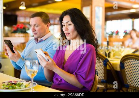 Ein erwachsenes Birazialpaar benutzt während des Mittagessens im Restaurant ein Telefon Stockfoto