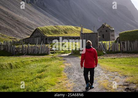 Ein Mann in roter Jacke, der auf einem ländlichen Pfad zum Wikingerdorf in der atemberaubenden Landschaft des Stokksnes-Tals und zum Vestrahorn-Berg in Island spaziert Stockfoto