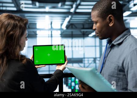 Mockup Tablet, das von Mitarbeitern im Rechenzentrum verwendet wird, die die Zahnraddiagnose für Rackbefestigungen überprüfen. Nahaufnahme eines Chroma-Schlüsselgeräts, das von IT-Experten im Team verwendet wird, die Brainstorming im Server-Hub durchführen Stockfoto