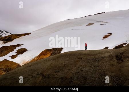 Panoramablick auf einen Wandermann in roter Jacke und den nebligen Kerlingarfjoll-Bergpfad inmitten von Wüste und schneebedecktem Gelände in Island Stockfoto