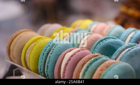 Nahaufnahme farbenfroher Macarons mit weißer Creme-Füllung unter sanfter Beleuchtung auf einer Arbeitsplatte mit verschwommenem Hintergrund und selektivem Fokus Stockfoto