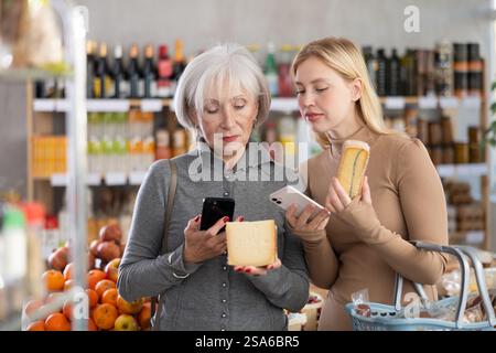 Die ältere Mutter und ihre Erwachsene Tochter scannen zusammen einen QR-Code auf einem Käseetikett, um das Verfallsdatum zu überprüfen Stockfoto
