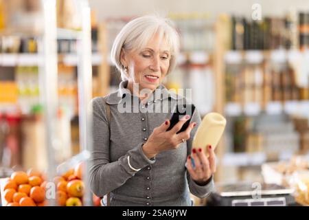 Ältere Käuferinnen scannen QR-Code auf Flaschenmayonnaise-Etikett in der Lebensmittelabteilung des Supermarktes Stockfoto