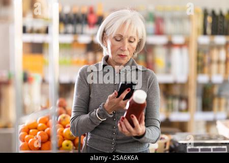 Ältere Käuferinnen scannen QR-Code auf Flaschenketchup-Etiketten in der Lebensmittelabteilung des Supermarktes Stockfoto