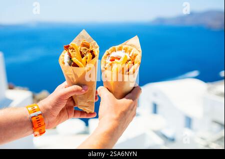 Griechische Gyros in Pita-Brot gewickelt, fotografiert gegen die traditionelle griechische Stadt mit weißen Häusern Stockfoto