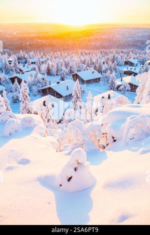 Atemberaubender Blick auf den Sonnenuntergang über Holzhütten und schneebedeckte Bäume im finnischen Lappland Stockfoto