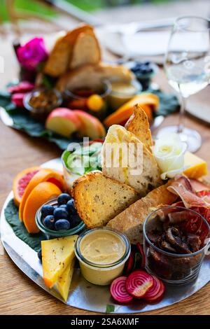 Eine lebendige Platte mit knusprigem Brot, verschiedenen Käsesorten, frischen Fruchtscheiben, Wurstwaren und cremigem Hummus, garniert mit bunten Rüben sl Stockfoto