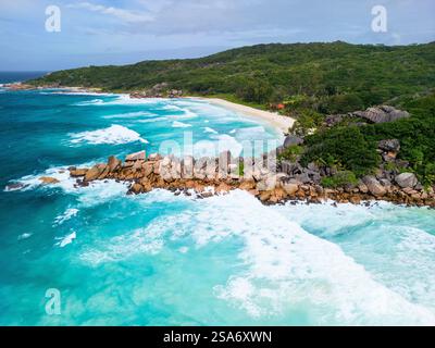 Luftaufnahme des Grand Anse Beach auf La Digue, Seychellen, mit türkisfarbenem Wasser, rauschenden Wellen, goldenem Sand, üppiges Grün und Granitfelsen für Stockfoto