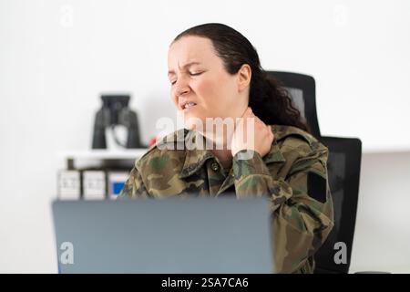 Schuss einer Soldatinnen, die Unbehagen in ihren Schultern hat, während sie an ihrem Schreibtisch sitzt Stockfoto