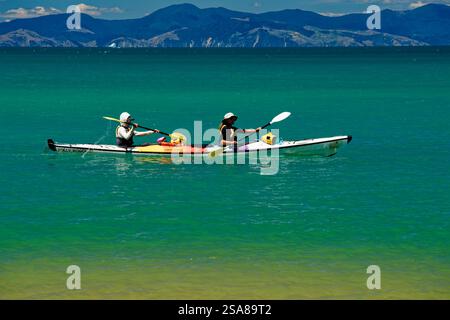 Abel Tasman National Park, Tasman District, Südinsel, Aotearoa / Neuseeland - 17. Januar 2025: Ein Paar paddelt mit einem weißen Meer Kajak in der lebhaften Landschaft Stockfoto
